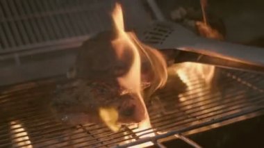 Close-up of big stake grilled on the big open fire and turned with tongs. Slow motion
