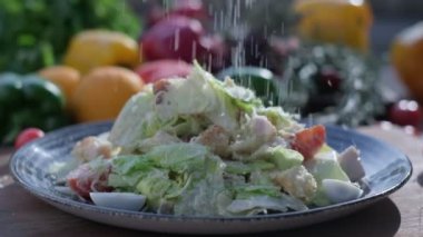 Close-up of coarsely chopped Caesar salad with chicken fillet in the ceramic dish is is sprinkled by hand with very finely grated cheese, which crumbles in all directions