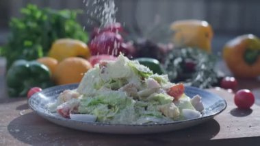 Close-up of coarsely chopped Caesar salad with chicken fillet in the ceramic dish is is sprinkled by hand with very finely grated cheese, which crumbles in all directions