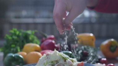 Close-up of coarsely chopped Caesar salad with chicken fillet in the ceramic dish is is sprinkled by hand with very finely grated cheese, which crumbles in all directions