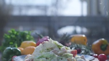 Close-up of coarsely chopped Caesar salad with chicken fillet in the ceramic dish is is sprinkled by hand with very finely grated cheese, which crumbles in all directions