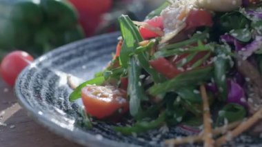 Close-up of coarsely chopped Caesar salad with chicken fillet in the ceramic dish is is sprinkled by hand with very finely grated cheese, which crumbles in all directions