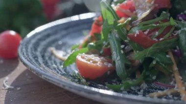 Close-up of coarsely chopped Caesar salad with chicken fillet in the ceramic dish is is sprinkled by hand with very finely grated cheese, which crumbles in all directions