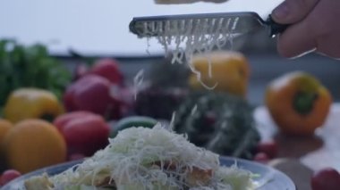 Close-up of hard cheese is grated on a small grater holding in hands. Slow motion