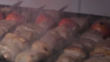 Close-up of lumpy kebab with tomato and ground kebab is grilled on the grill. There is a lot of smoke from the grill