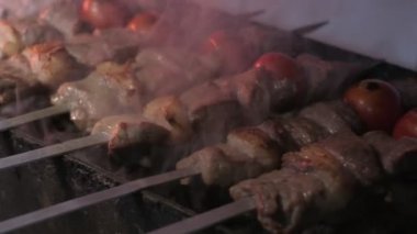 Close-up of lumpy kebab with tomato and ground kebab is grilled on the grill. There is a lot of smoke from the grill