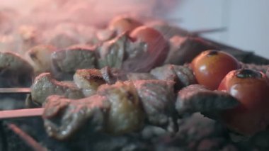 Close-up of lumpy kebab with tomato and ground kebab is grilled on the grill. There is a lot of smoke from the grill