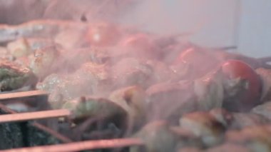 Close-up of lumpy kebab with tomato and ground kebab is grilled on the grill. There is a lot of smoke from the grill