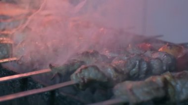 Close-up of lumpy kebab with tomato and ground kebab is grilled on the grill. There is a lot of smoke from the grill