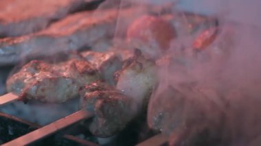 Close-up of lumpy kebab with tomato and ground kebab is grilled on the grill. There is a lot of smoke from the grill