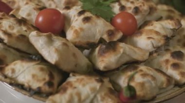 Close-up of bunch of samsa Central Asian buns on the big dish decorated with cherry tomatoes and hot pepper