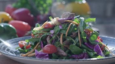 Close-up of fresh salad made of red cabbige, tomatoes, onions, basil, arugula and pieces of fried meat. Fresh veggies on the back