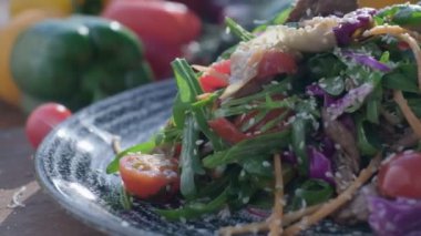 Close-up of fresh salad made of red cabbige, tomatoes, onions, basil, arugula and pieces of fried meat. Fresh veggies on the back