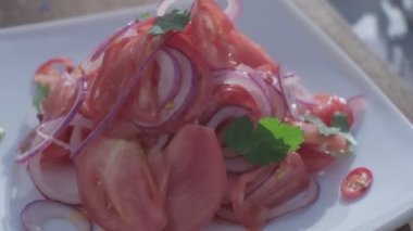 Close-up of fresh salad made of red cabbige, tomatoes, onions, basil, arugula and pieces of fried meat. Fresh veggies on the back
