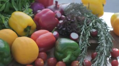 Close-up of fresh veggies including red, green and yellow bell peppers, cherry tomatoes and juniper on the wooden cooking board