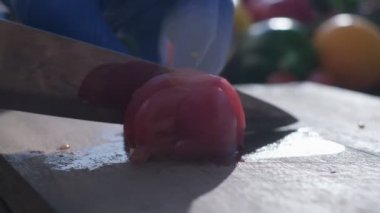 Close-up of tomato cut by the knife on the wooden cooking board. The hands of a cook are in blue rubber gloves