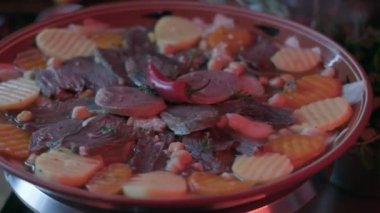 Close-up of national Kazakh dish Beshbarmak made of veggies, dough and horsemeat served in deep clay dish with hot red pepper on top