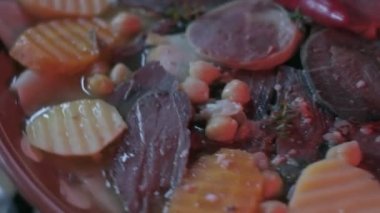 Close-up of national Kazakh dish Beshbarmak made of veggies, dough and horsemeat served in deep clay dish with hot red pepper on top