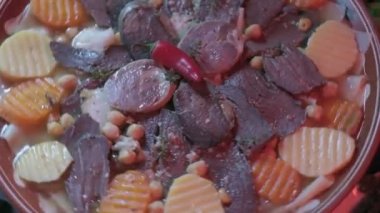 Close-up of national Kazakh dish Beshbarmak made of veggies, dough and horsemeat served in deep clay dish with hot red pepper on top