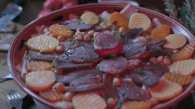 Close-up of national Kazakh dish Beshbarmak made of veggies, dough and horsemeat served in deep clay dish with hot red pepper on top