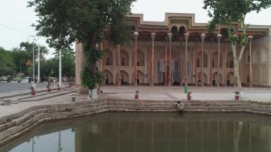 And old eastern building with high wooden carved columns on the pediment placed near the artificial pond. Filmed in old Bukhara city on cloudy day.
