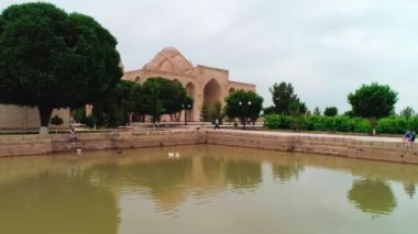 Drone cam takes off from the platform in front of the pool of memorial complex of Bahouddin Naqshband near Bukhara. It flies through the square up the Naqshband mausoleum and next we see an old