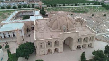 Drone camera is flying around Bahouddin Naqshband mausoleum in eponymous memorial complex near Bukhara. The cemetery and madrasah are also visible in the frame. Filmed on a cloudy day
