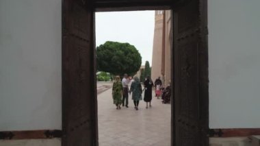Inner-yard of memorial complex of Bahouddin Naqshband near Bukhara shoot by drone. A lot of visitors nearby. Camera flies to the stone well surrounded by oriental brickwork and ornamental tiles