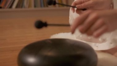 Young woman meditates doing yoga playing on the steel tongue drum. Hang drum music instrument. Close-up