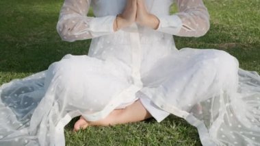 Young woman meditating doing yoga in the park on a sunny day, slow motion, close-up
