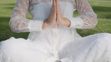 Young woman meditating doing yoga in the park on a sunny day, slow motion, close-up