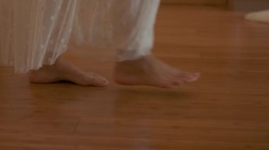 A young woman walks barefoot on the parquet in a sunny room. Slow motion.