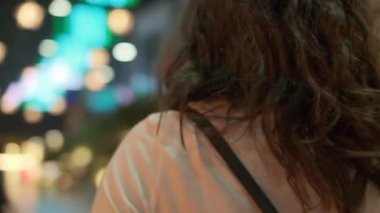 A young beautiful woman walks alone along a brightly lit night street.