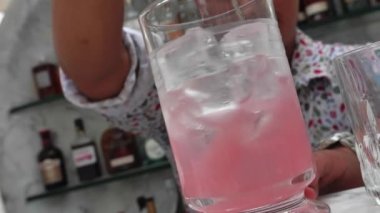 Barman puts ice into coctail shaker. He is wearing white summer shirt with doodles. Slow motion.