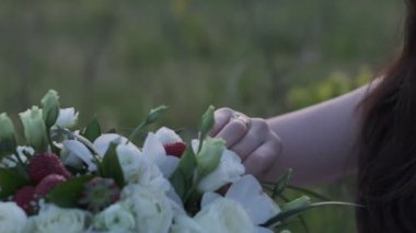 Womans hand touches a bouquet of white roses and strawberries close-up, slow motion