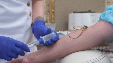 Blood sample is taken from vein by nurse wearing blue gloves