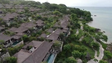 Flight of a drone over a tropical cottage village on the seashore during high tide