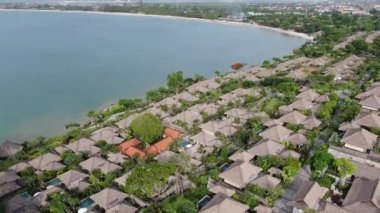 Flight of a drone over a tropical cottage village on the seashore during high tide