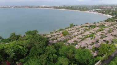 Flight of a drone over a tropical cottage village on the seashore during high tide