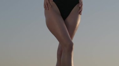 A brunette in a black swimsuit stands barefoot on the sand dune in the desert. Slow motion.