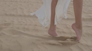 Young girl in a fluttering white dress dancing barefoot on the sand in the desert. Slow motion. Close up.