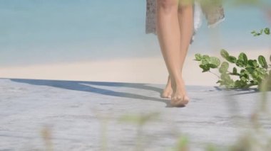 Legs of a young brunette woman in a bikini slowly walking along the shore. Slow motion.