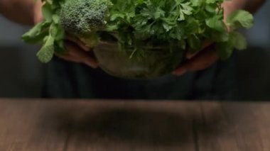 Male hands put a bowl of greens broccoli, cilantro, mint etc on the table. Close up slow motion