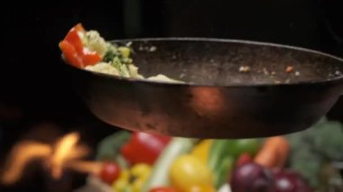 The pan-flip of veggies above the grills strong flame. Close up slow motion