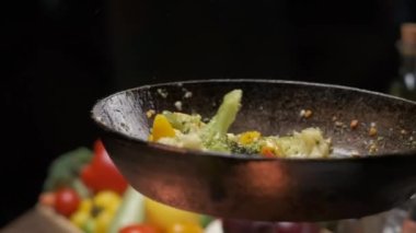 The pan-flip of veggies above the grills strong flame. Close up slow motion