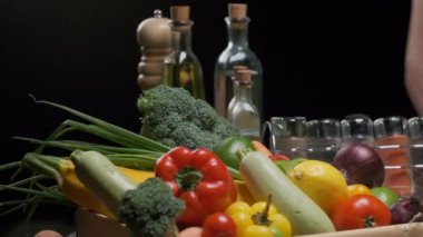 Fresh vegetables and greens, bottles with olive oil and vinegar, some spice jars on the kitchen table. Slow motion