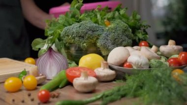 Bowl of greens and broccoli, plate with mushrooms and cherry tomatoes and some fresh veggies on the table. Slow motion