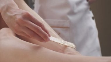 Close-up of depilatory gel being applied on womans legs by wooden stick