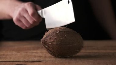 Man tries to chop a coconut on the table. Black background, slow motion