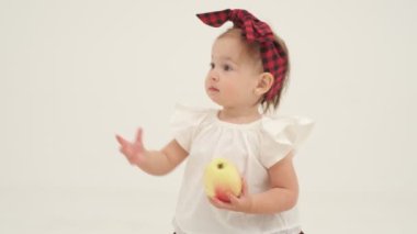 Ekose saç bandı ve etekli küçük kız büyük elma tutuyor. Ağır çekimde kapat